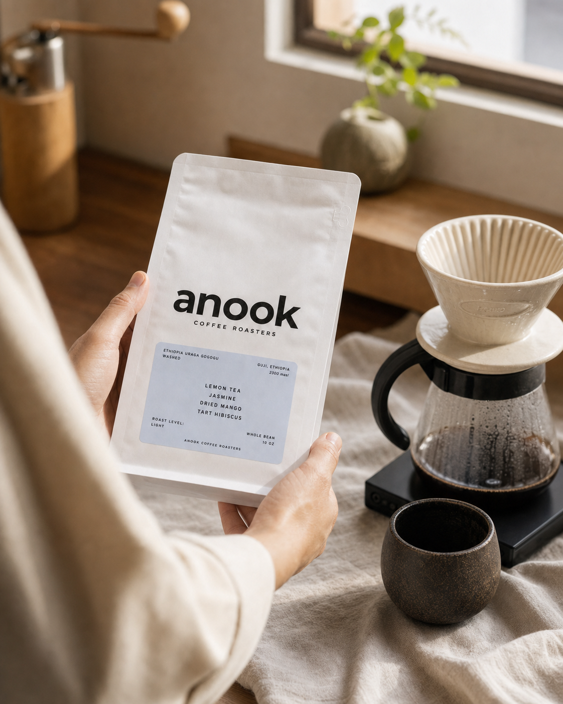 Hands holding an Anook Ethiopia Uraga Gogogu coffee bag beside a pour-over setup