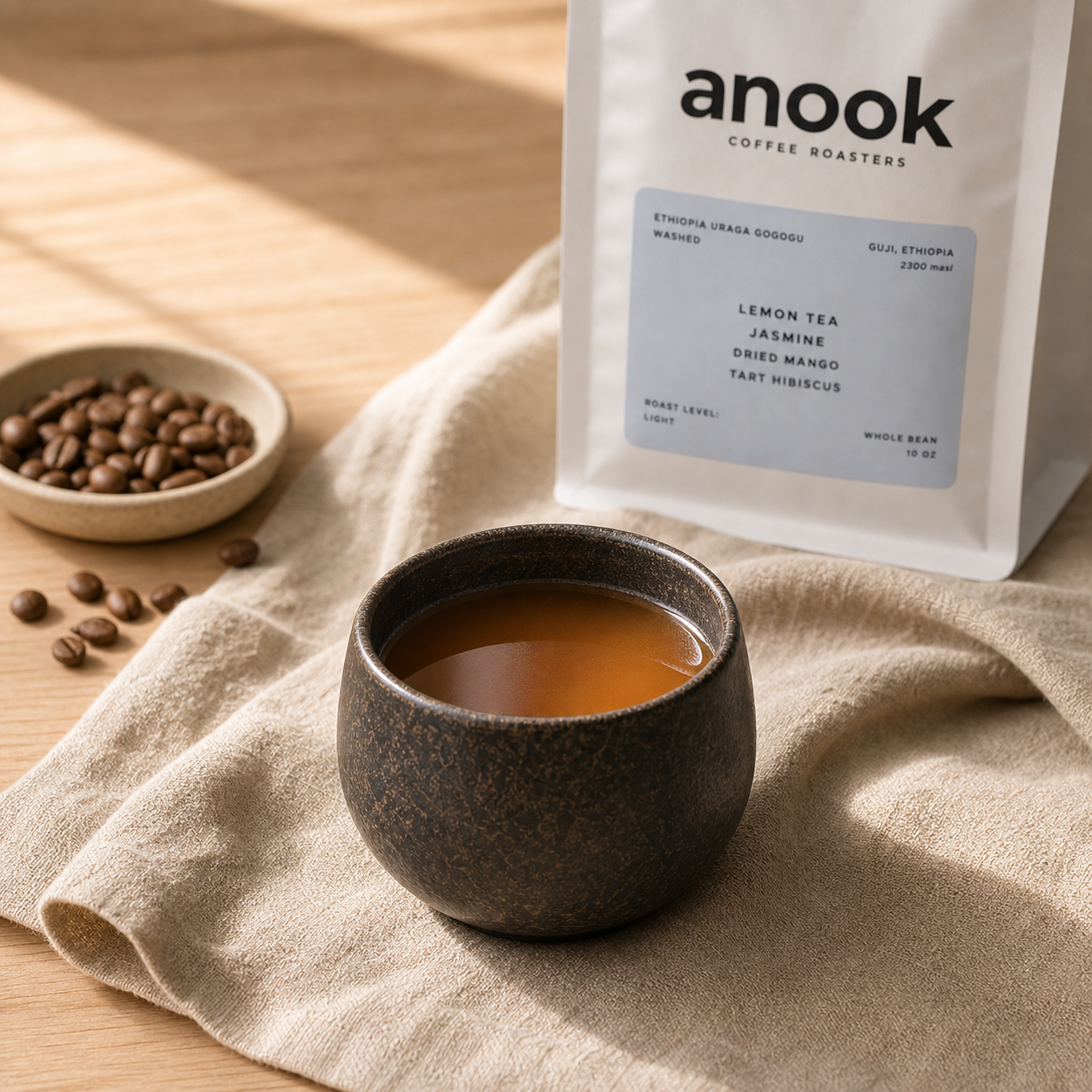 Brewed filter coffee in a dark ceramic cup with Anook coffee in the background